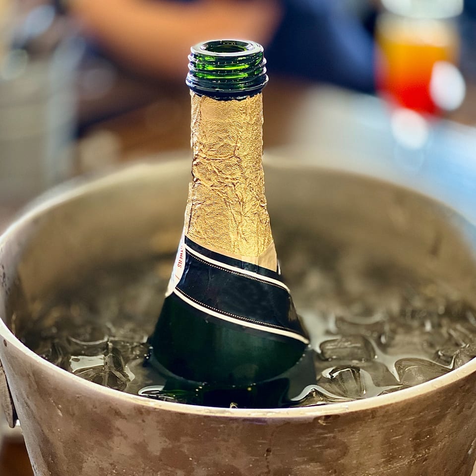 A champagne bottle with a gold foil top chills in a bucket of ice.
