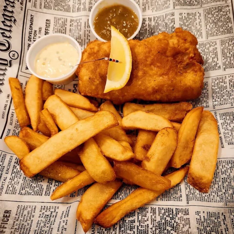 Golden-brown fish and chips with lemon and two dipping sauces, served on newspaper.