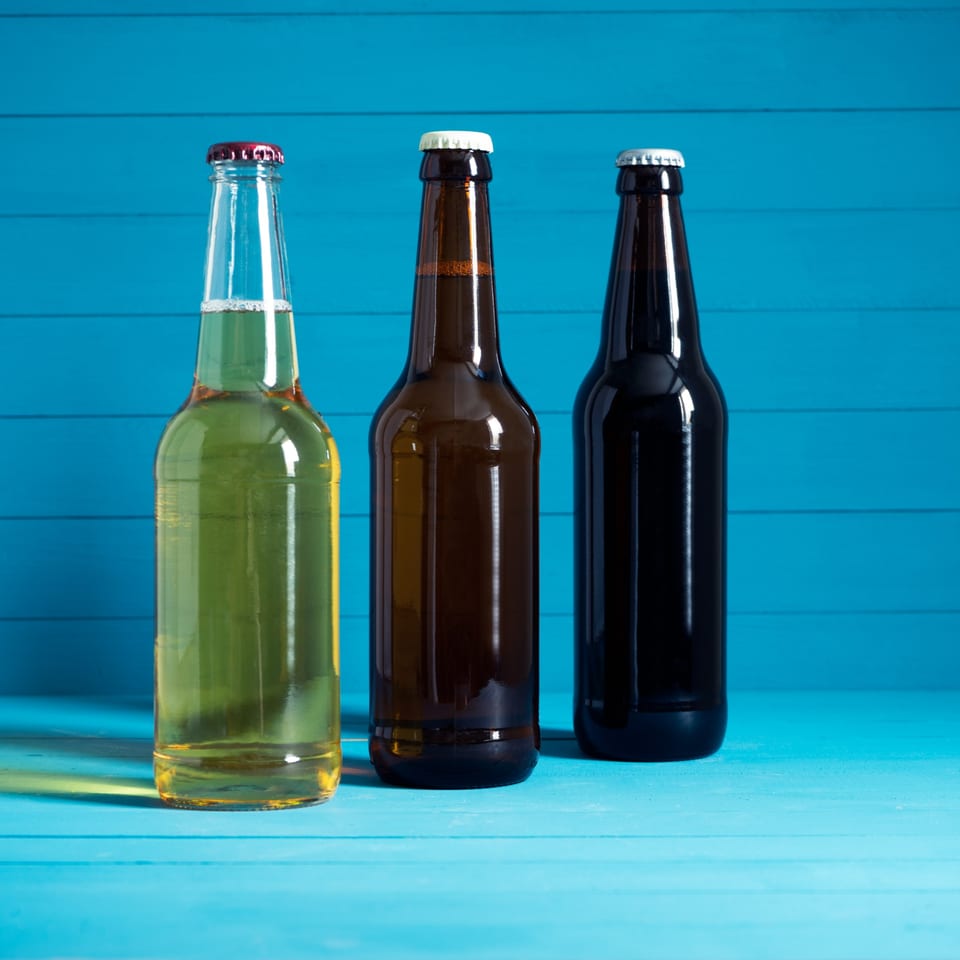 Three beer bottles, light, amber, and dark, on a blue wooden surface.
