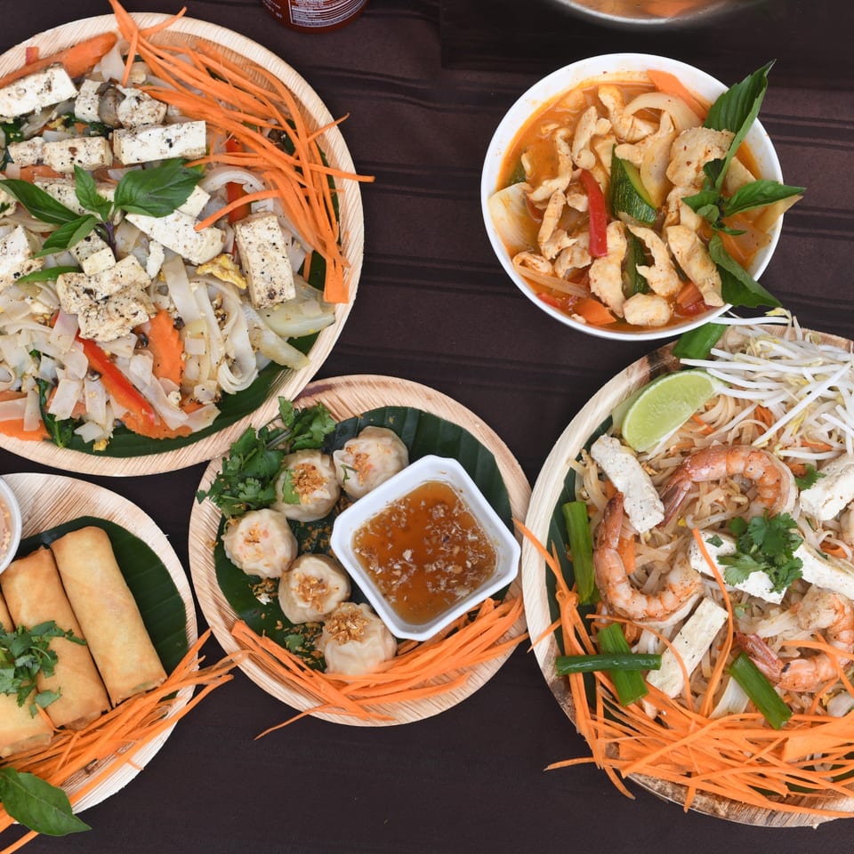 Assortment of Thai dishes including pad see ew, curry, dumplings, spring rolls, and pad Thai.