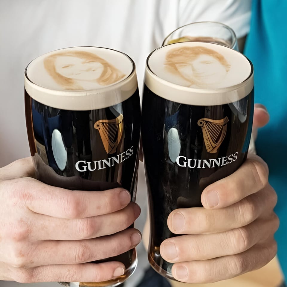 Two hands holding Guinness pints with custom foam art portraits on top, at The British Embassy.
