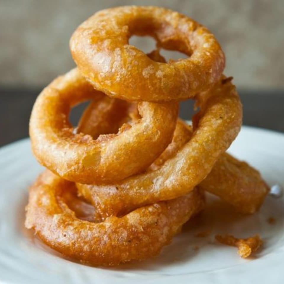 A stack of golden-brown, crispy onion rings on a white plate, ready to be served.