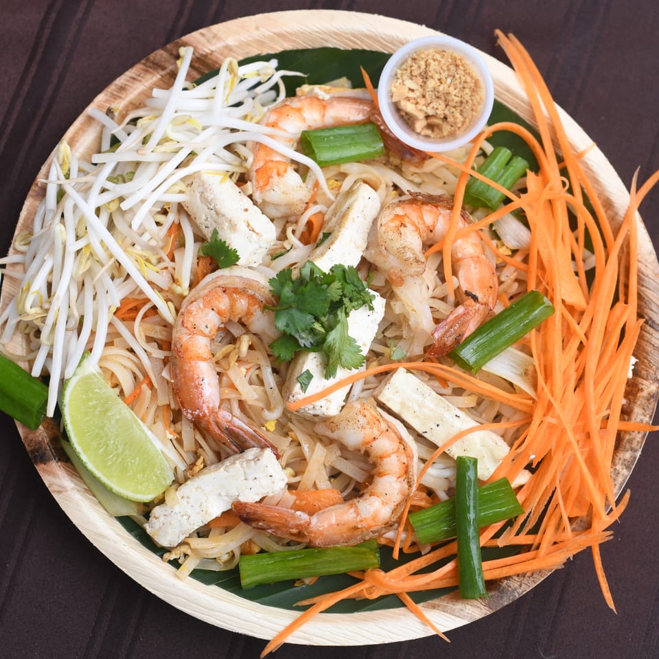 Pad Thai with shrimp, tofu, bean sprouts, carrots, and lime on a wooden plate.