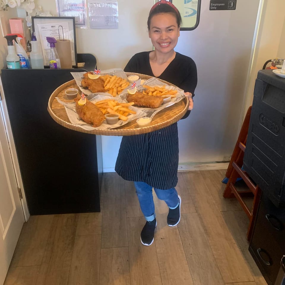 Smiling woman holding a large tray with three servings of British fish and chips.