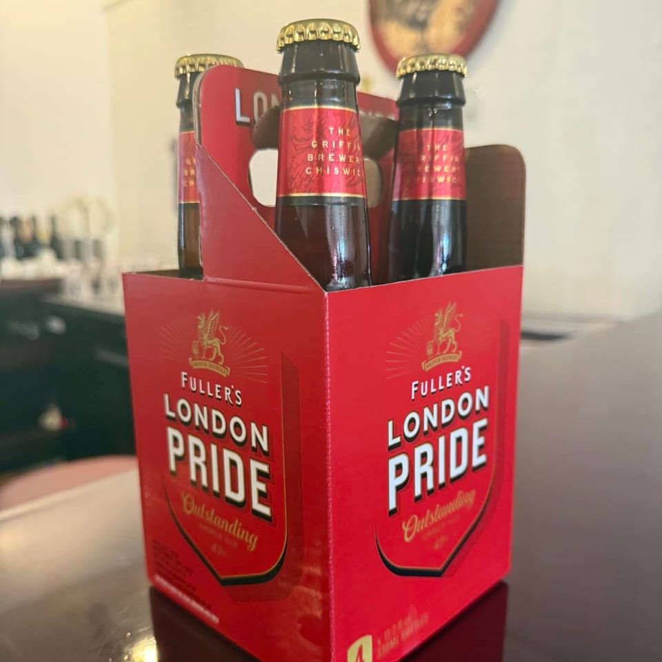 A red six-pack of Fuller's London Pride beer bottles sits on a dark table.