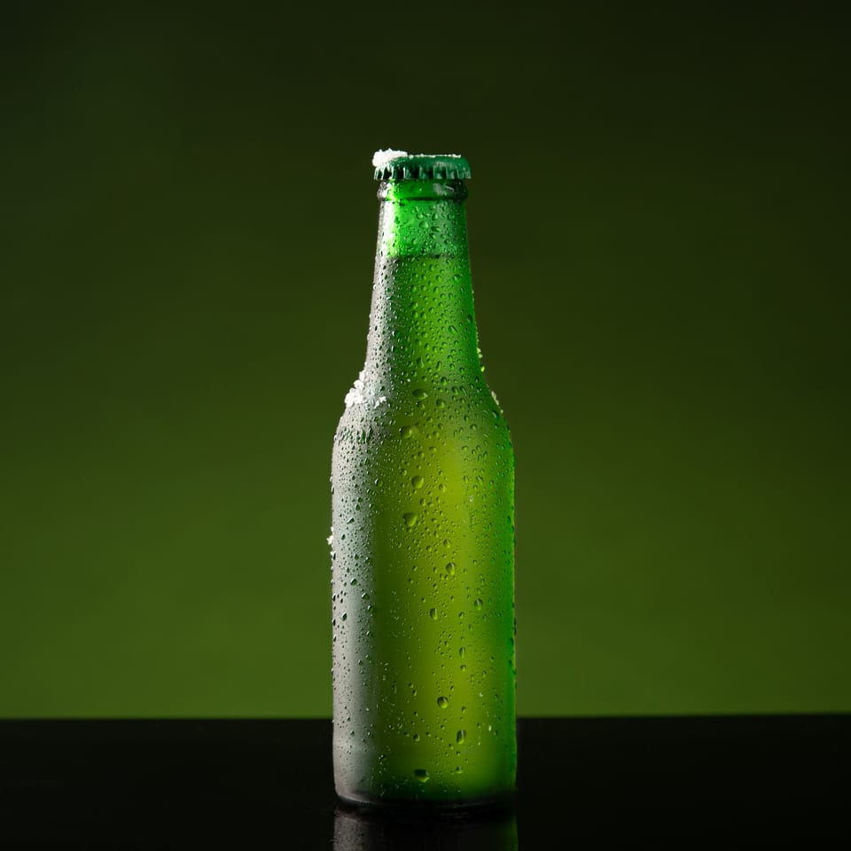 Chilled green beer bottle with condensation and a frosty cap against a dark green background.