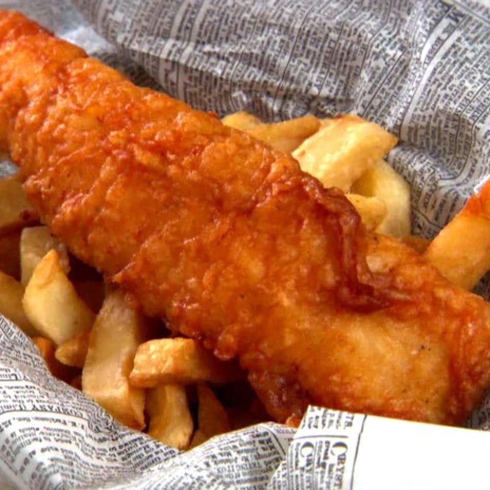 Golden-brown battered fish and thick-cut chips served in newspaper-style wrapping from The British Embassy Fish and Chips.