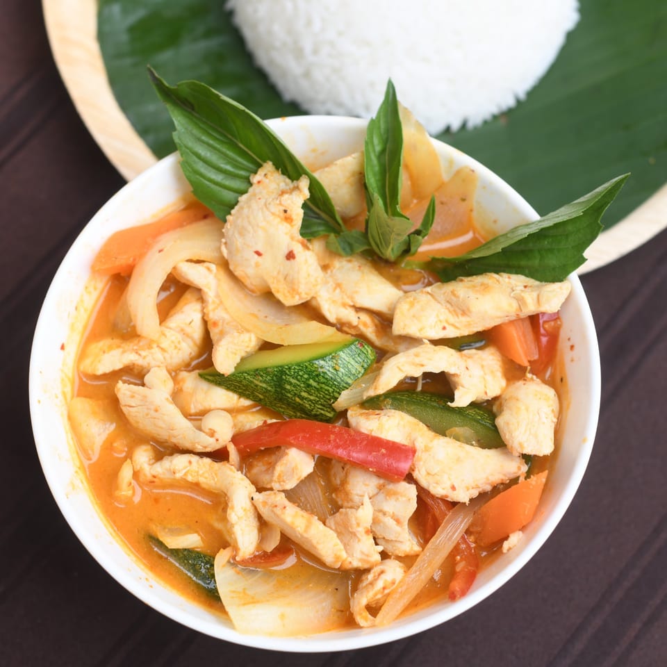 A bowl of chicken curry with vegetables and basil, served with white rice.